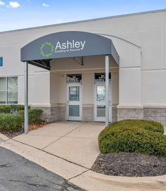 Exterior front entrance showing Ashley Addiction Treatment signage, covered awning entry, landscaping, and facility building facade