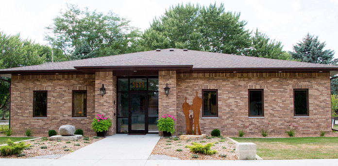 Exterior of brick treatment facility showing central entrance, multiple windows, landscaped grounds with plantings and rocks.