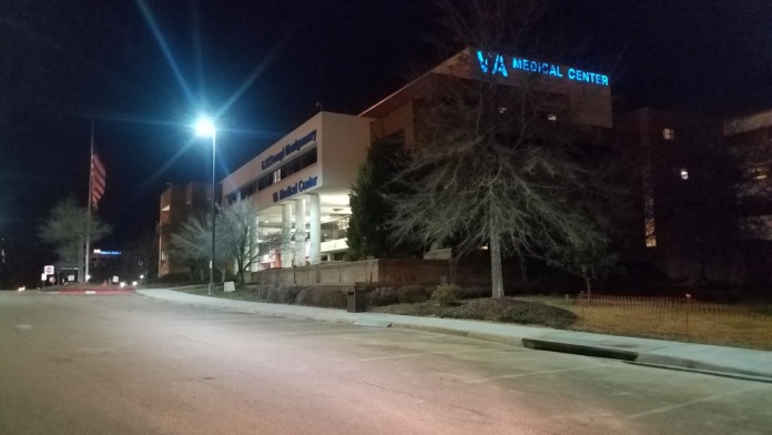 Exterior view of VA Medical Center at night showing multi-story building with blue neon signage, parking area, and landscaping.