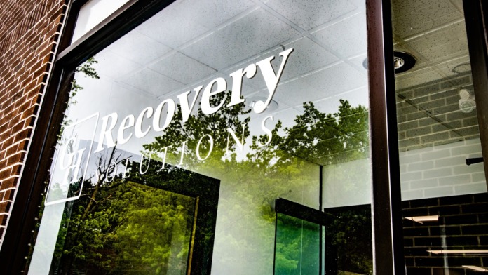 Exterior storefront entrance with glass doors, Recovery Solutions logo visible on window, dark frames, and brick walls