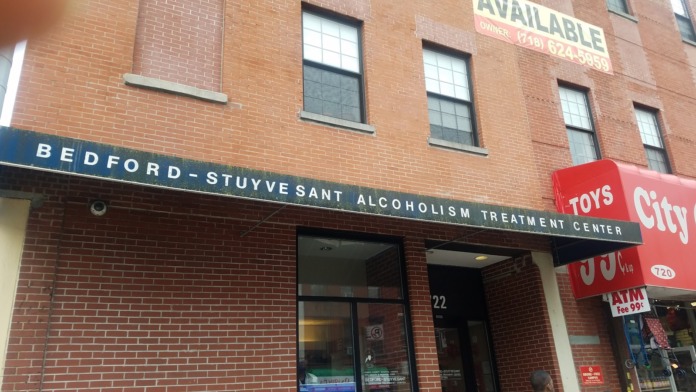 Exterior storefront of Bedford-Stuyvesant Alcoholism Treatment Center with dark awning and glass entrance doors on Myrtle Avenue