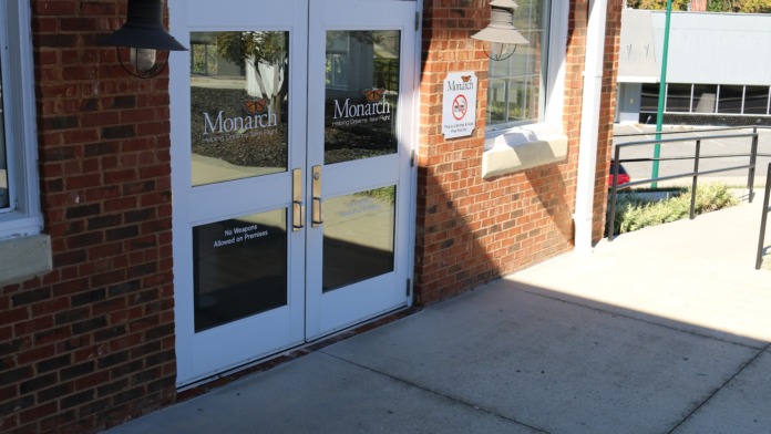 Exterior entrance with light blue double doors, Monarch signage, and red brick building facade with landscaping