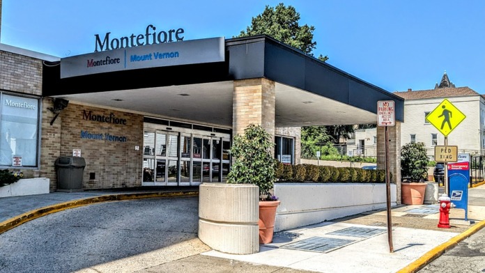 Exterior showing Montefiore Mount Vernon medical facility main entrance with covered portico, glass doors, and parking area