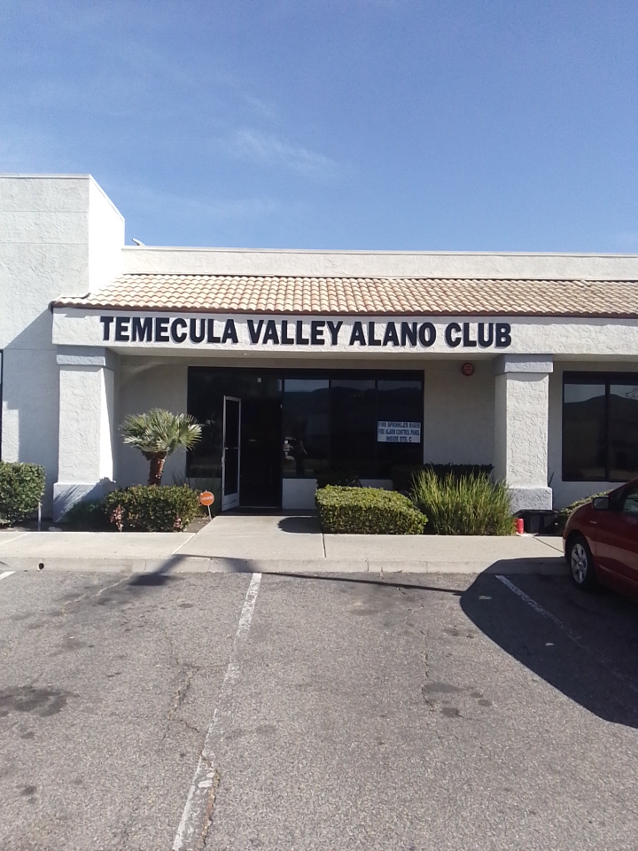 Exterior front entrance of Temecula Valley Alano Club with white stucco facade, dark windows, and landscaped grounds
