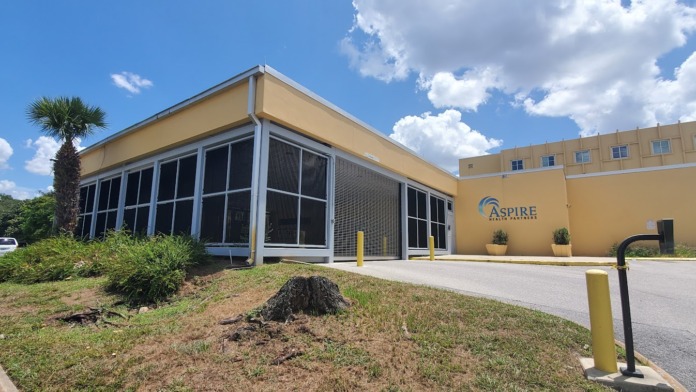 Exterior view of Aspire Health Partners ANCHOR facility showing main entrance, yellow building facade, and landscaped grounds with parking area