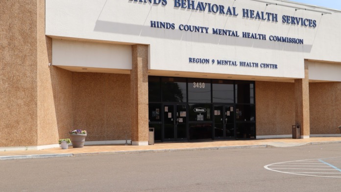 Exterior front facade of HINDS Behavioral Health Services facility showing brown brick building, main entrance doors, and institutional signage