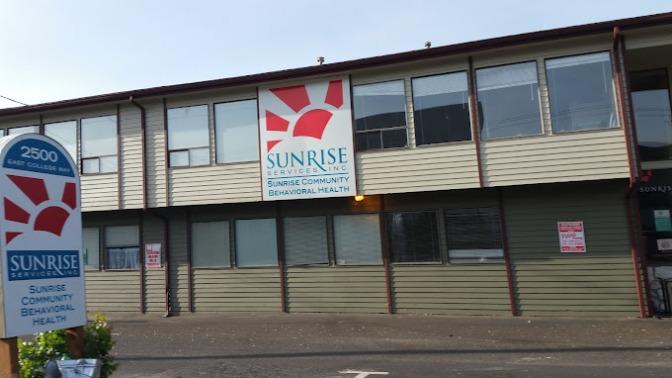 Exterior of Sunrise Community Mental Health building with main entrance, signage, and parking area visible