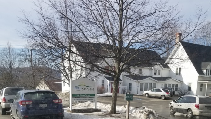 Exterior view of Kennebec Behavioral Health facility showing main entrance sign, white building, parking area with vehicles, and bare trees