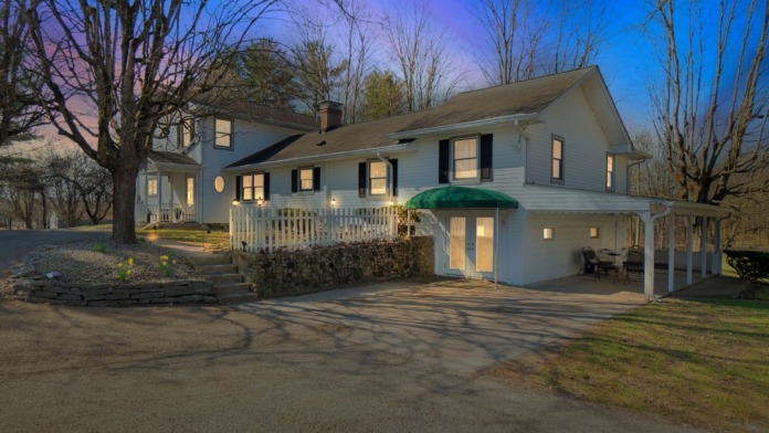 Exterior view of white farmhouse-style treatment facility with covered porch, landscaped grounds, and driveway at dusk