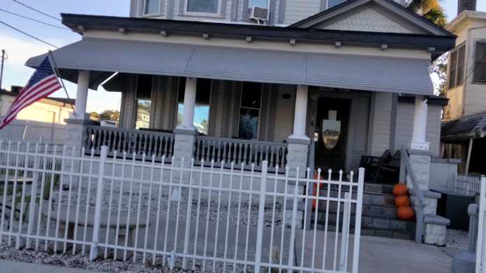 Exterior view of white Victorian treatment center building with front porch, white railings, and American flag.
