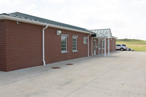 Exterior of single-story brick treatment facility building with entrance doors, windows, concrete parking area, and open grounds.
