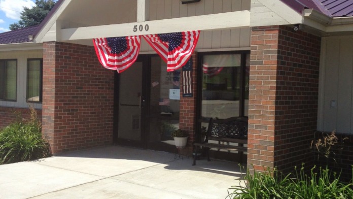 Exterior front view of treatment center building with brick construction, purple metal roof, main entrance, and patriotic decorations.
