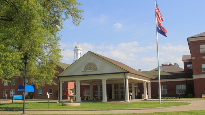 Exterior of medical facility with columned portico, brick construction, flagpole, and manicured grounds