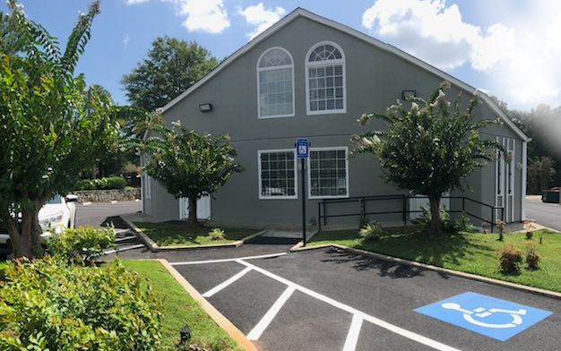 Exterior view of gray treatment facility building with main entrance, handicap accessible parking space, and landscaped grounds