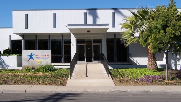Exterior of Teen Challenge facility showing modern white building with main entrance, landscaping, and parking area