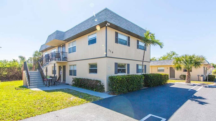 Exterior view of two-story treatment facility with tan and stone facade, palm trees, and manicured lawn