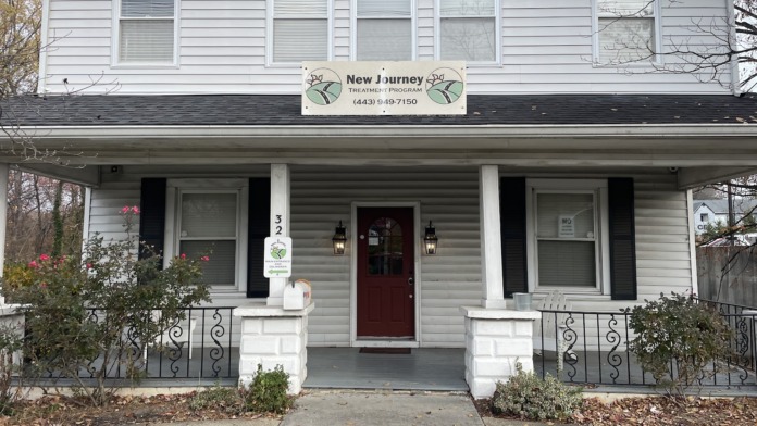 Exterior view of New Journey Treatment Program facility showing white two-story building with red entrance door, covered porch, and facility signage