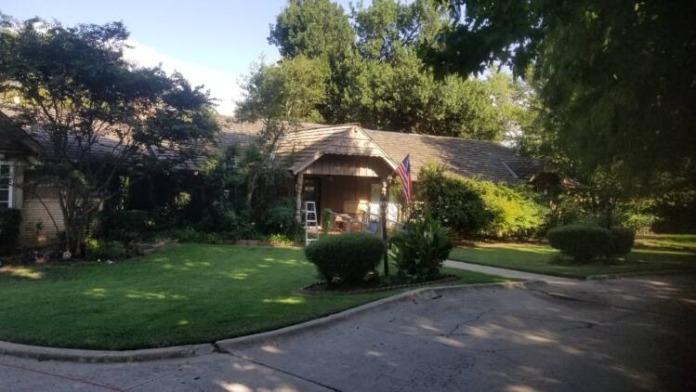 Exterior brick building with covered entrance portico, landscaped grounds, and mature trees