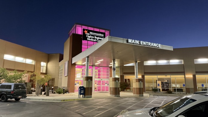 Exterior of medical center showing main entrance with bright pink accent signage, parking area, and landscaping
