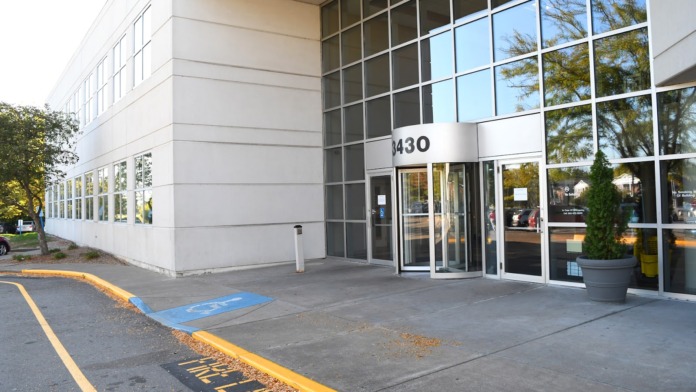 Exterior of modern white and glass building showing entrance, accessible parking, and landscaping.
