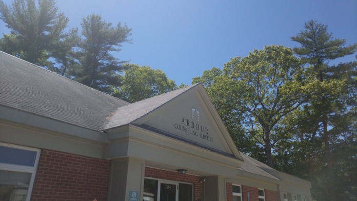 Exterior view of Arbour Counseling Services brick building with entrance, signage, landscaping, and parking area