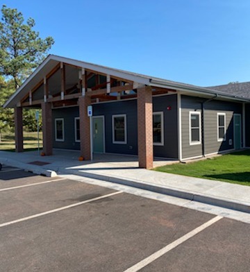 Exterior view of single-story treatment facility with covered entrance, dark siding, and paved parking area on clear day