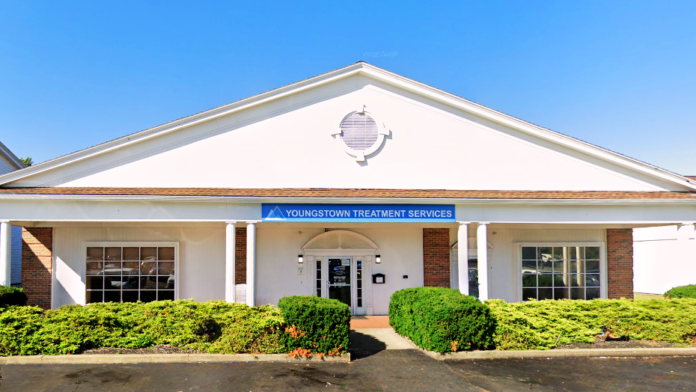 Exterior of treatment facility showing main entrance with columns, blue signage, and parking lot