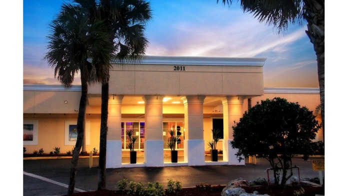 Exterior front entrance with lit columns and palm trees at dusk