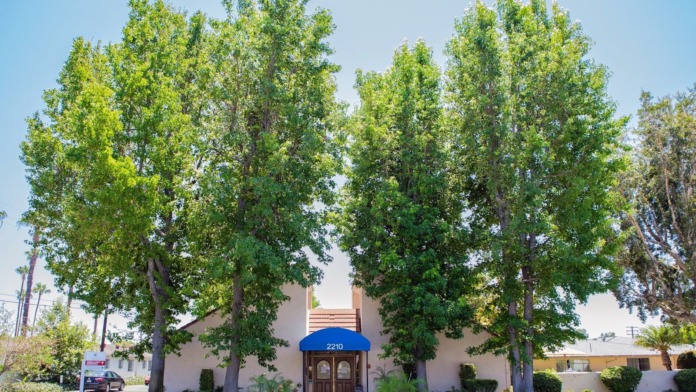 Exterior view of facility entrance with blue awning, address 2210, landscaped grounds with mature trees