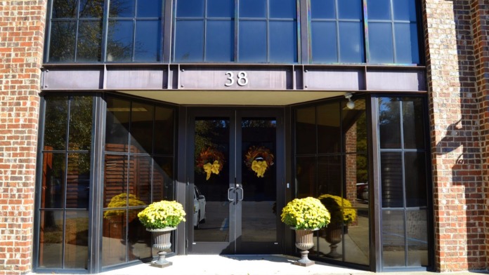 Exterior entrance of The Highlands Treatment Center showing brick facade, large windows, number 38, and yellow chrysanthemum planters