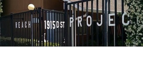 Exterior view of REACH Project facility entrance showing black metal gate with white lettering displaying facility name and address on D Street