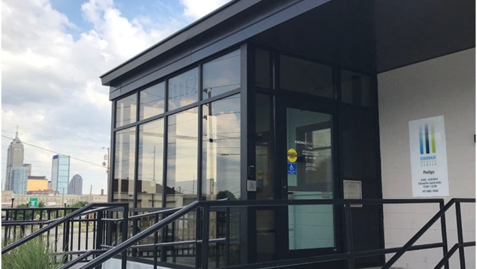 Exterior view of modern entrance featuring black-framed glass doors, metal railings, and Eskenazi Health Center Pedigo signage on white wall