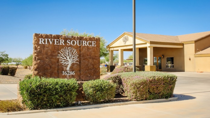 Exterior front entrance showing The River Source facility sign with tree logo and address number 16286, tan building with covered entry