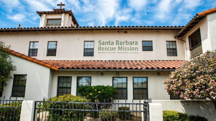 Exterior view of Santa Barbara Rescue Mission building with white stucco facade, red tile roof, cross, landscaping, and facility name signage