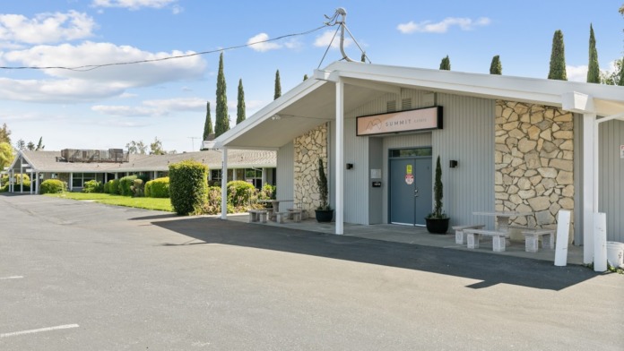 Exterior front entrance of Summit Estate Recovery featuring stone and metal paneling, covered portico, and landscaping with cypress trees