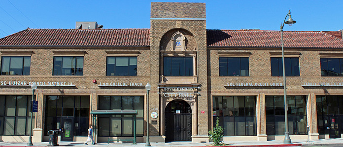 Exterior view of brick building with arched entrance, multiple storefronts, windows, and street-level access