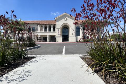 Exterior of white two-story VA facility building with arched entrance, landscaped grounds with ornamental plantings, and driveway approach.