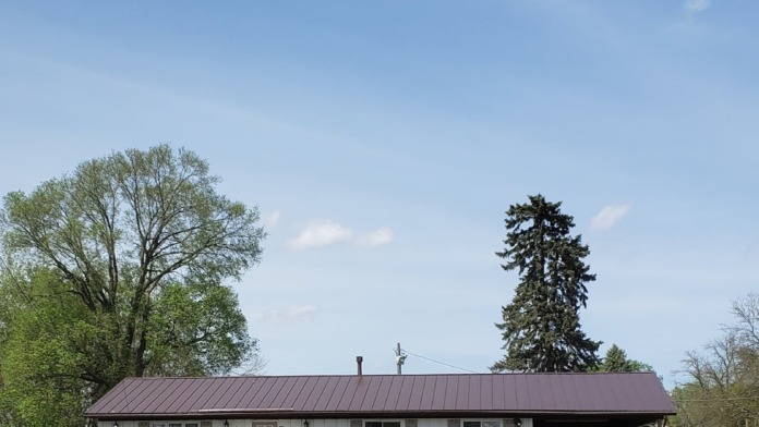 Exterior view of single-story white treatment center building with dark roof, landscaped grounds, paved parking area, and mature trees.