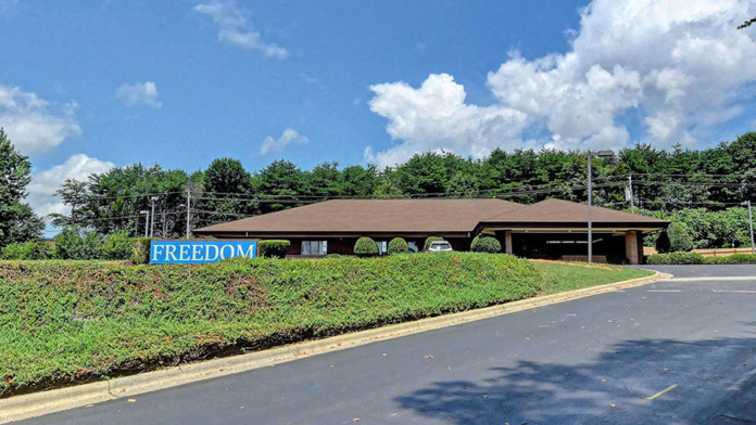 Exterior front view of Freedom Detox treatment center with blue FREEDOM sign, landscaped grounds, and brick building facade