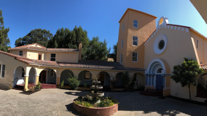 Exterior view of multi-building treatment facility with Spanish-style architecture, arched entryways, courtyard, and landscaping under clear blue sky