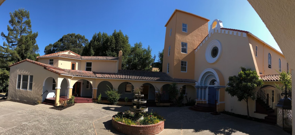 Exterior view of multi-building treatment facility with Spanish-style architecture, arched entryways, courtyard, and landscaping under clear blue sky