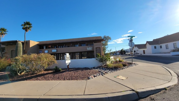 Exterior view of Next Step Counseling building showing tan and white facade, dark roof, palm trees, and desert landscaping on East Speedway Boulevard