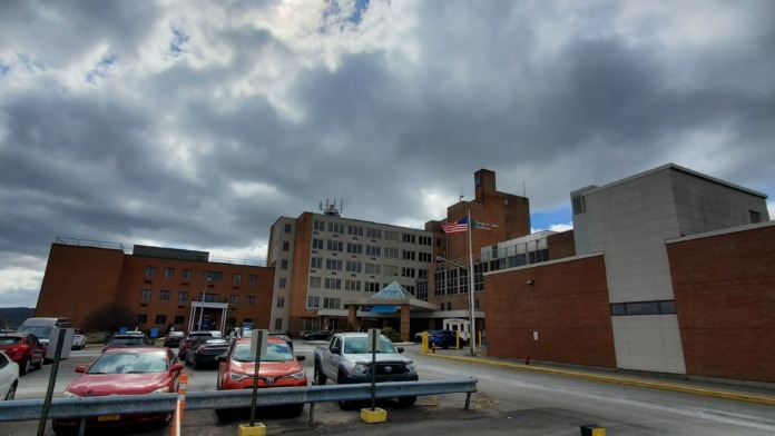 Exterior view of multi-story brick healthcare facility with parking area, vehicles, and cloudy sky