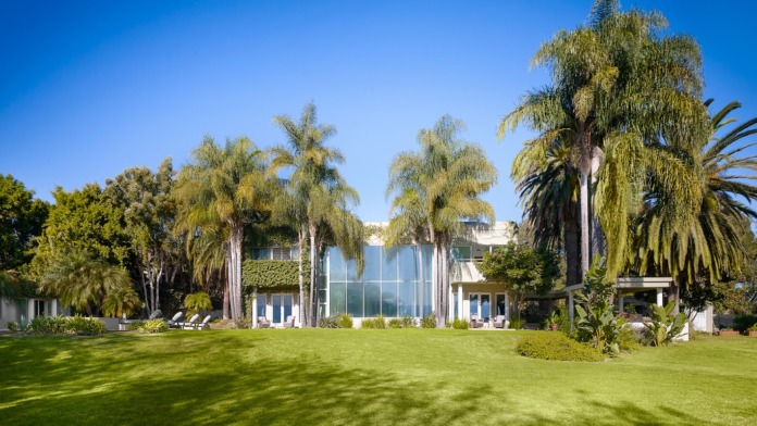 Exterior view of modern white building with extensive landscaping, palm trees, and manicured lawn