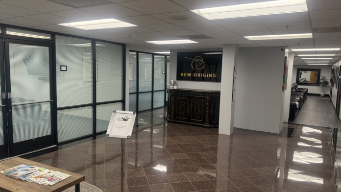 Interior lobby with polished flooring, New Origins branded signage, glass partition walls, and information materials displayed