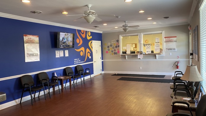 Interior lobby with reception desk, blue and orange walls, Spero Health signage, multiple waiting chairs, and wooden flooring