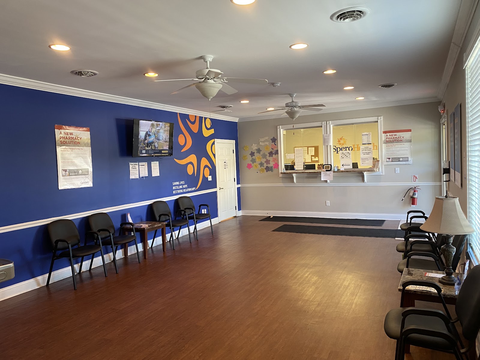 Interior lobby with reception desk, blue and orange walls, Spero Health signage, multiple waiting chairs, and wooden flooring
