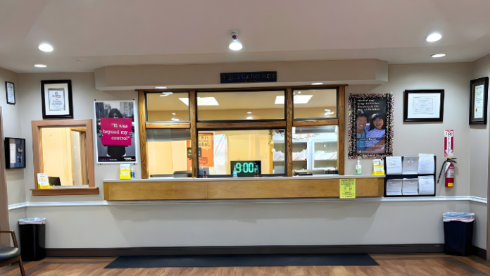Interior lobby with service counter, wooden fixtures, framed artwork, digital clock display, recessed ceiling lights, and professional reception space