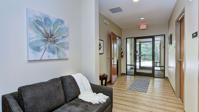 Interior lobby with black sofa, blue flower artwork, glass doors leading outside, blue rug, and wooden flooring