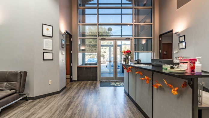 Interior lobby featuring black reception desk with flowering arrangement, large windows overlooking grounds, framed credentials on walls, and seating area